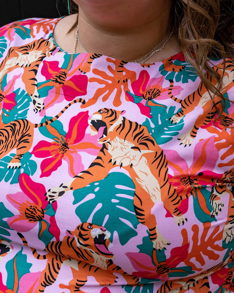 Close up of Natalie wearing Tiger Lily Stretch Belted Tea Dress with Pockets. The baby pink dress has an all over print of tigers with flowers and leaves.