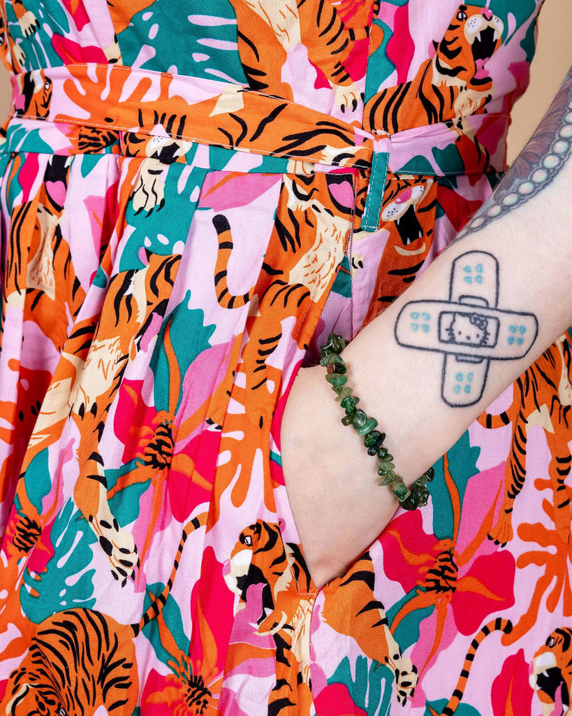 Close up of Faeryn's hand in the pocket of the Tiger Lily Stretch Belted Tea Dress with Pockets. The baby pink dress has an all over print of tigers with flowers and leaves.