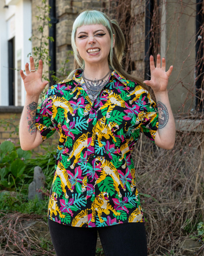 Model poses playfully in a bold tiger print shirt by Run & Fly featuring yellow tigers, tropical leaves and pink flowers. Ethically made unisex fashion from British slow fashion brand Run & Fly.