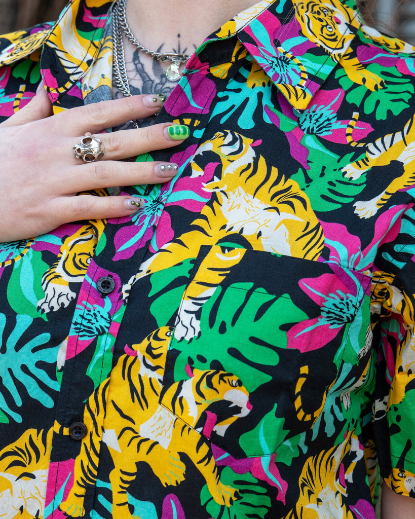 Close-up of Run & Fly’s colourful tiger print shirt showing vibrant yellow tigers, green monstera leaves, and pink flowers. Ethically made bold unisex clothing by UK slow fashion brand Run & Fly.