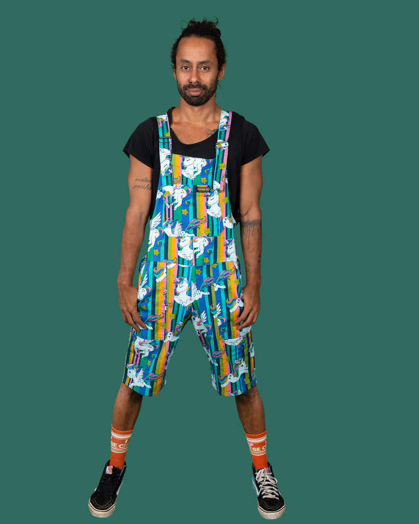 Full front pose of a model in Run & Fly's colourful unicorn short overalls. The vibrant pattern features stripes and stars, paired with a black t-shirt, emphasizing the brand's fun and sustainable fashion.