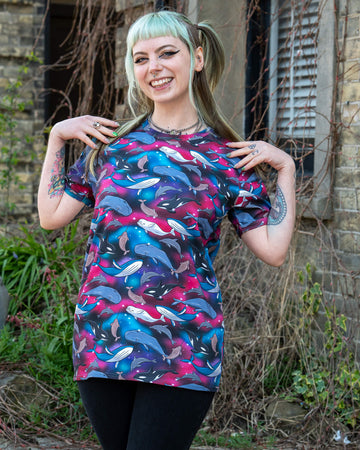 Person posing joyfully in the Run & Fly Cosmic Sea T Shirt, with an all-over print of sea creatures like dolphins and whales on a bright galaxy-style background. A colourful, comfy, short sleeve top from a small UK ethical fashion brand.