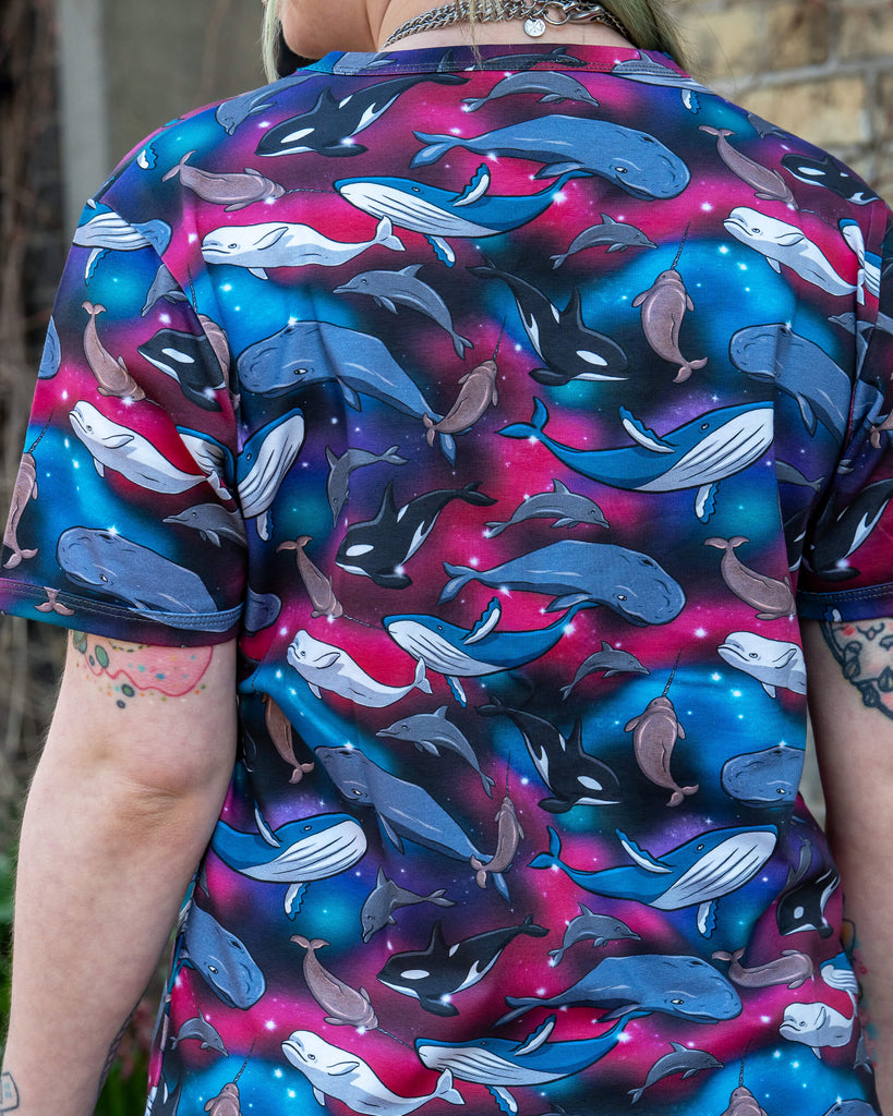 Back view of a person wearing a Run & Fly Cosmic Sea Short Sleeve T Shirt with a colourful all-over print of whales, dolphins, narwhals, and orcas on a galaxy background. The design by Kate Beaumont features bold shades of pink, blue, and purple. Ethical slow fashion made in the UK.
