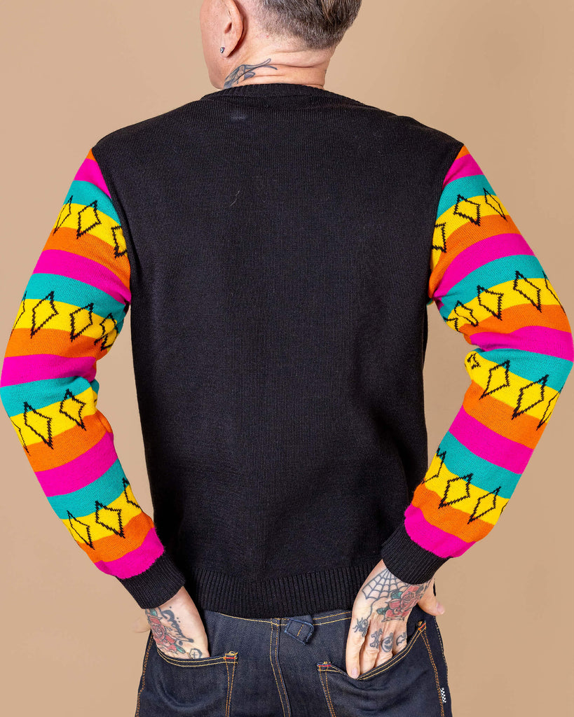 James is wearing the Run & Fly x Katie Abey Winter Weirdo Jumper with cats club pinafore underneath. She is facing forward with one hand on her head, the other hand by her side whilst looking to the left. The jumper has rainbow sleeves with black cuffs and sparkles, the chest is black and white christmas sparkles and patterns striped down it with 'Winter Weirdo' written in the centre with a rainbow behind the text to match the sleeves.