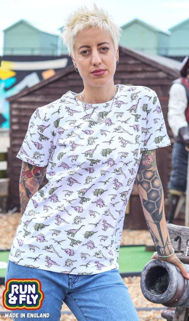 Yo is stood in a mini golf course area wearing the white jurassic dinosaur ringer print tshirt with blue denim jeans. They are facing forward posing with one hand resting on the golf course and the other behind them. Photo is cropped from the hips up.