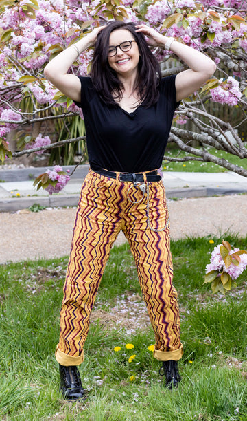 Amy is wearing the 90's zigzag straight leg high waisted jeans with a long sleeve black tshirt and yellow black boots looking smiley in front of a blossom tree