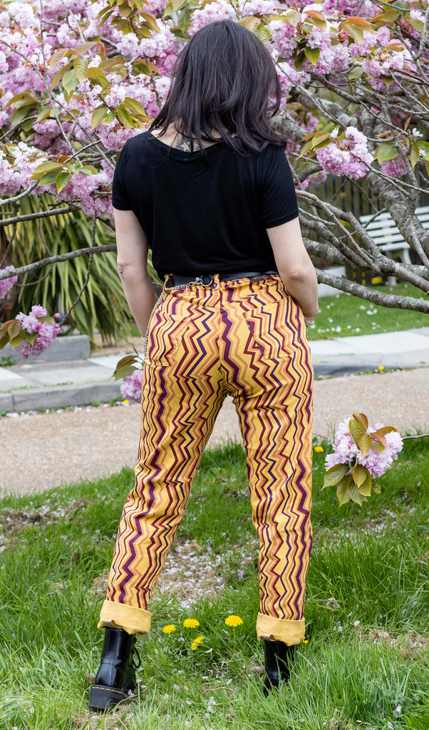 Amy is wearing the 90's zigzag straight leg high waisted jeans with a long sleeve black tshirt and yellow black boots looking to the back front of a blossom tree