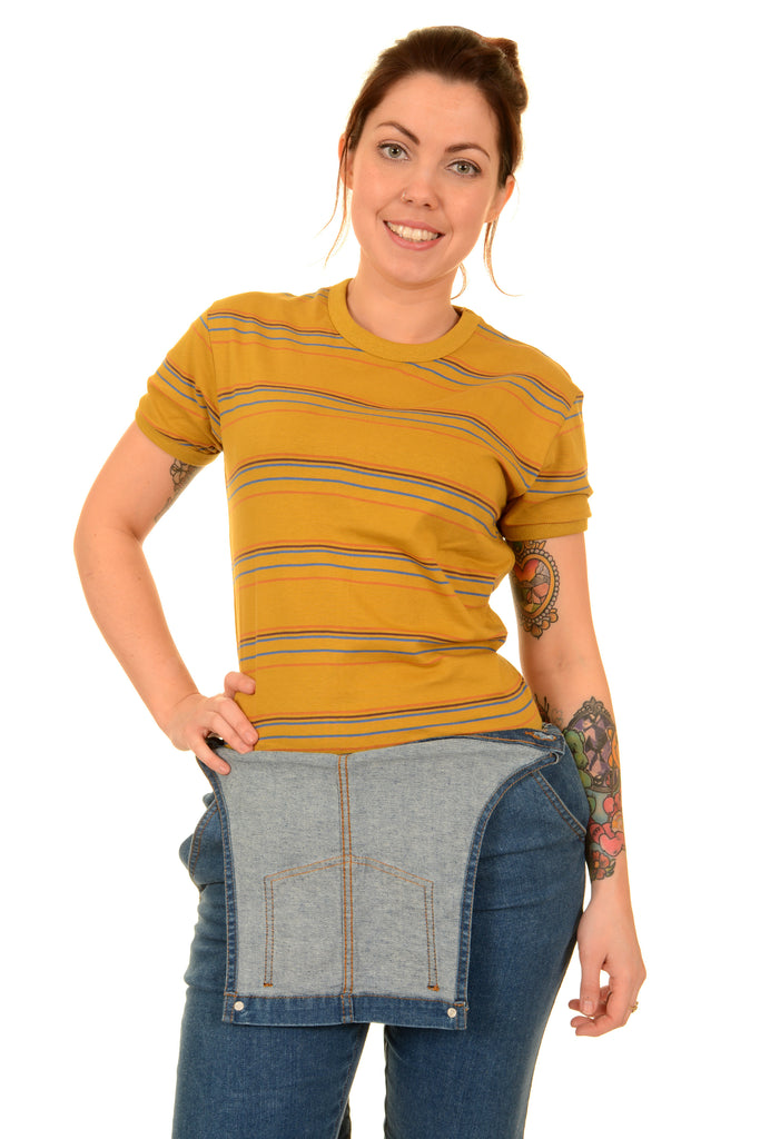 Model is stood in front of a white studio background wearing the sunset stripe retro tshirt with unbuttoned blue dungarees. They are facing forward with one hand on their hip and the other by their side whilst smiling to camera. Photo is cropped from the knees up.