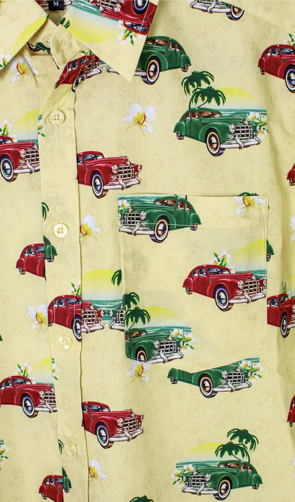 Close up shot of the Cuba short sleeve shirt showing green and red retro cars with palm trees and beach scenery and white tropical flowers on a pastel yellow background.