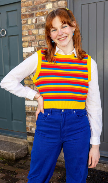 Tasha is a smiley female red haired model with a fringe wearing a white shirt and cobalt jeans with a striped yellow, blue, orange and red tank top. She is stood in a mews in Hove