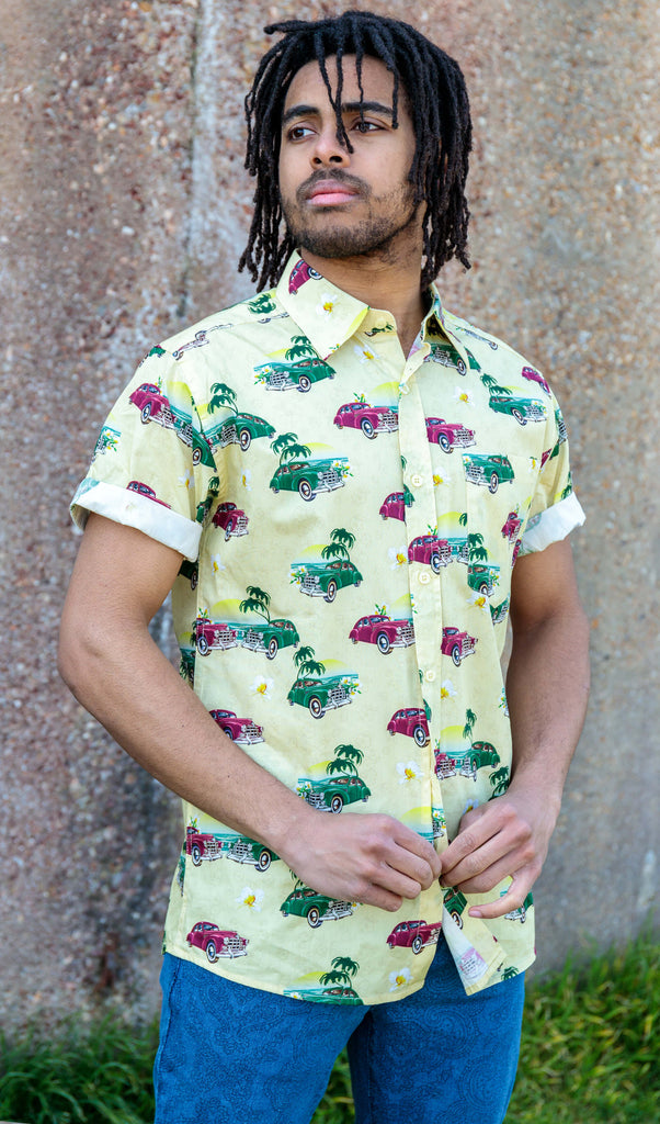 Model is stood outside in front of a concrete wall wearing the Cuba short sleeve shirt with denim paisley flares. They are facing towards the camera with both hands doing up the bottom button whilst looking off to the left. Photo is cropped from the thighs up.