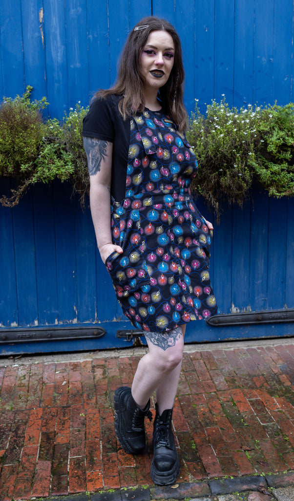 Alice a brown haired tattooed model wearing a fairy lights pinafore  dress by Run & Fly against a blue door