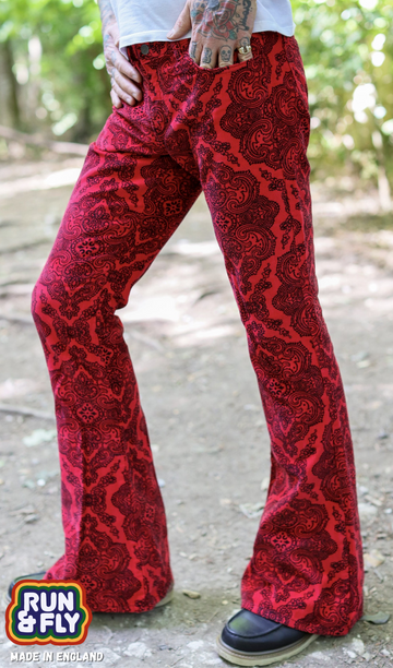 Model is stood in a wooded area wearing the Hendrix paisley corduroy retro bell bottom flares with a white short sleeve tshirt and brown boat shoes. They are facing to the left and posing with one leg out to the side to highlight the flares. Photo has been cropped from the waist down.