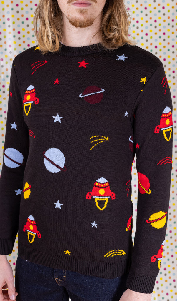 Close up photo of the front of the retro rocket outer space jumper paired with dark denim jeans, modelled by Jack in front of a multicoloured polka dot background.